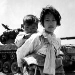 a famous photo of a young girl carrying an infant in front of a tank during the korean war